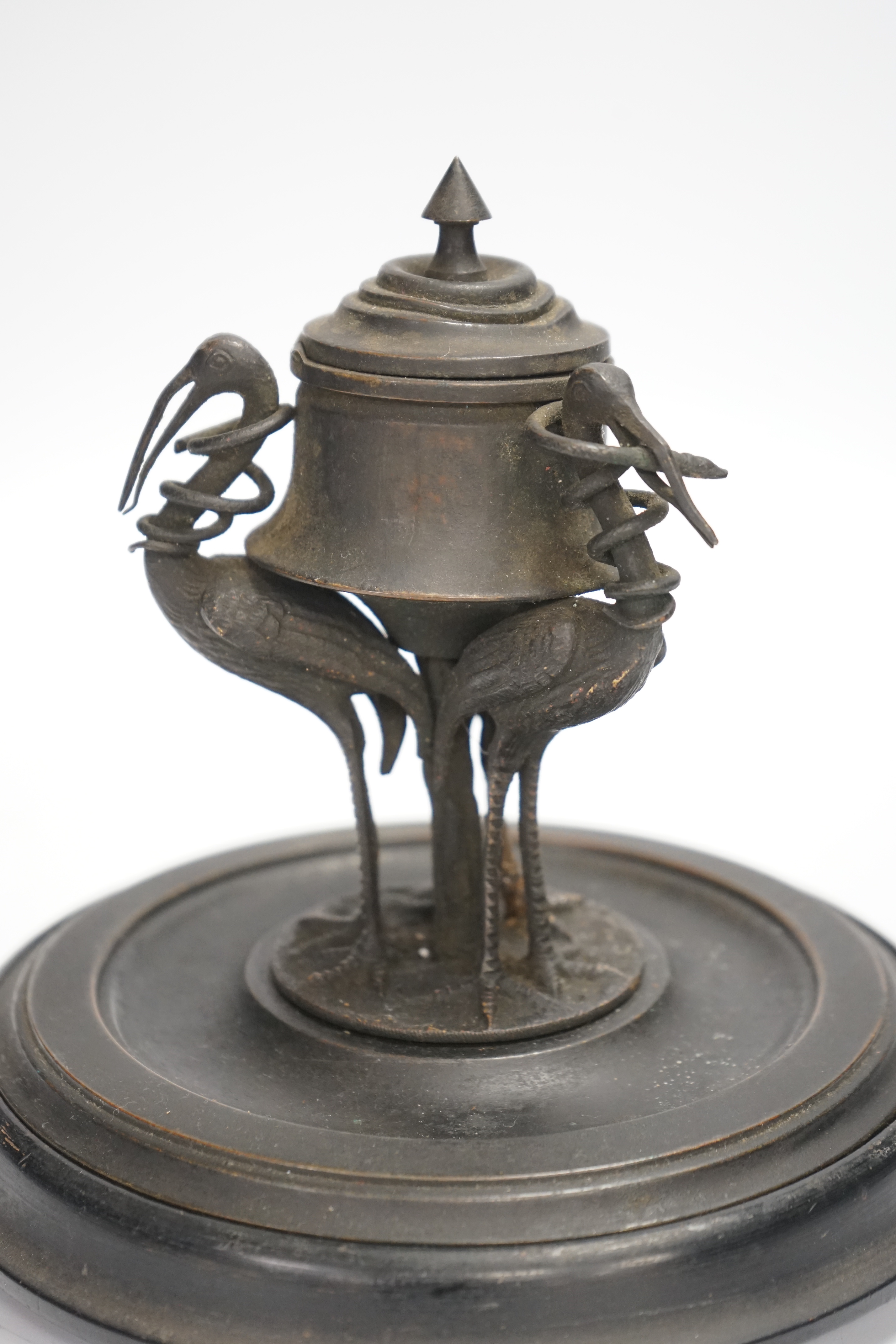 A late 19th century patinated metal inkwell, modelled with three cranes on an ebonised pine base, 18cm